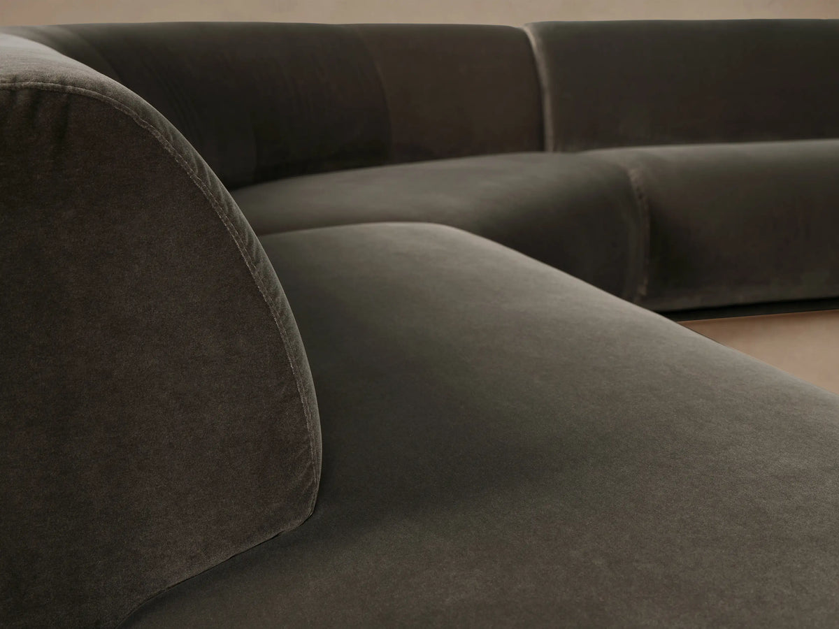 Gianni three-piece curved bumper sectional in dark olive velvet, on a wooden floor against a light wall.