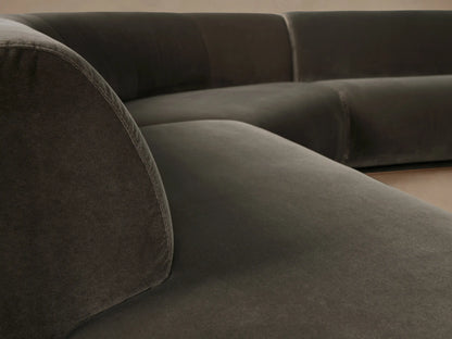 Gianni three-piece curved bumper sectional in dark olive velvet, on a wooden floor against a light wall.