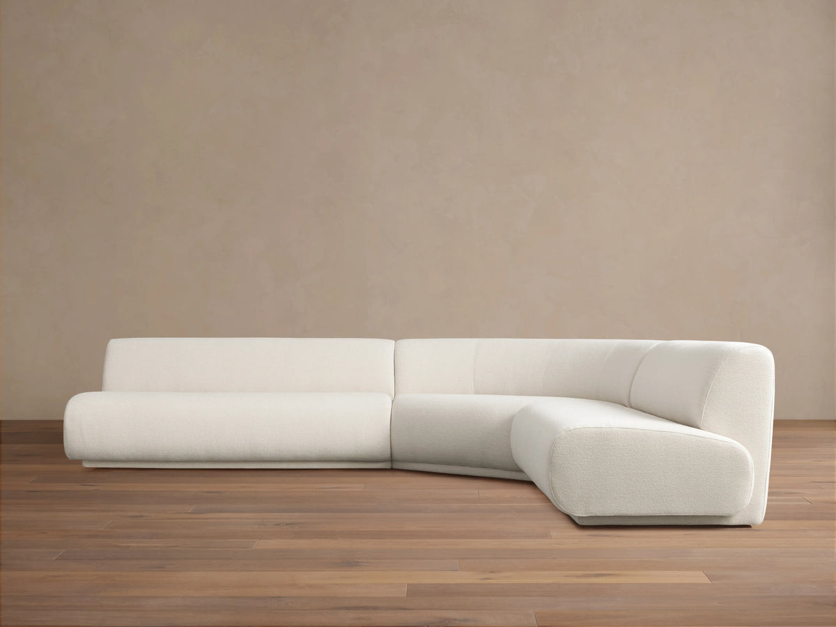 Gianni Three-Piece Corner Sectional in white fabric, featuring a modern, minimalist design. Set on a light wood floor against a beige wall.