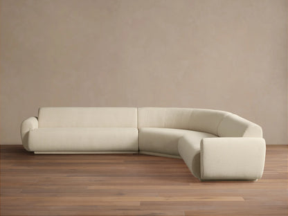 Gianni Three-Piece Corner Sectional. Off-white curved L-shaped sofa with soft texture on a wooden floor, against a beige wall.