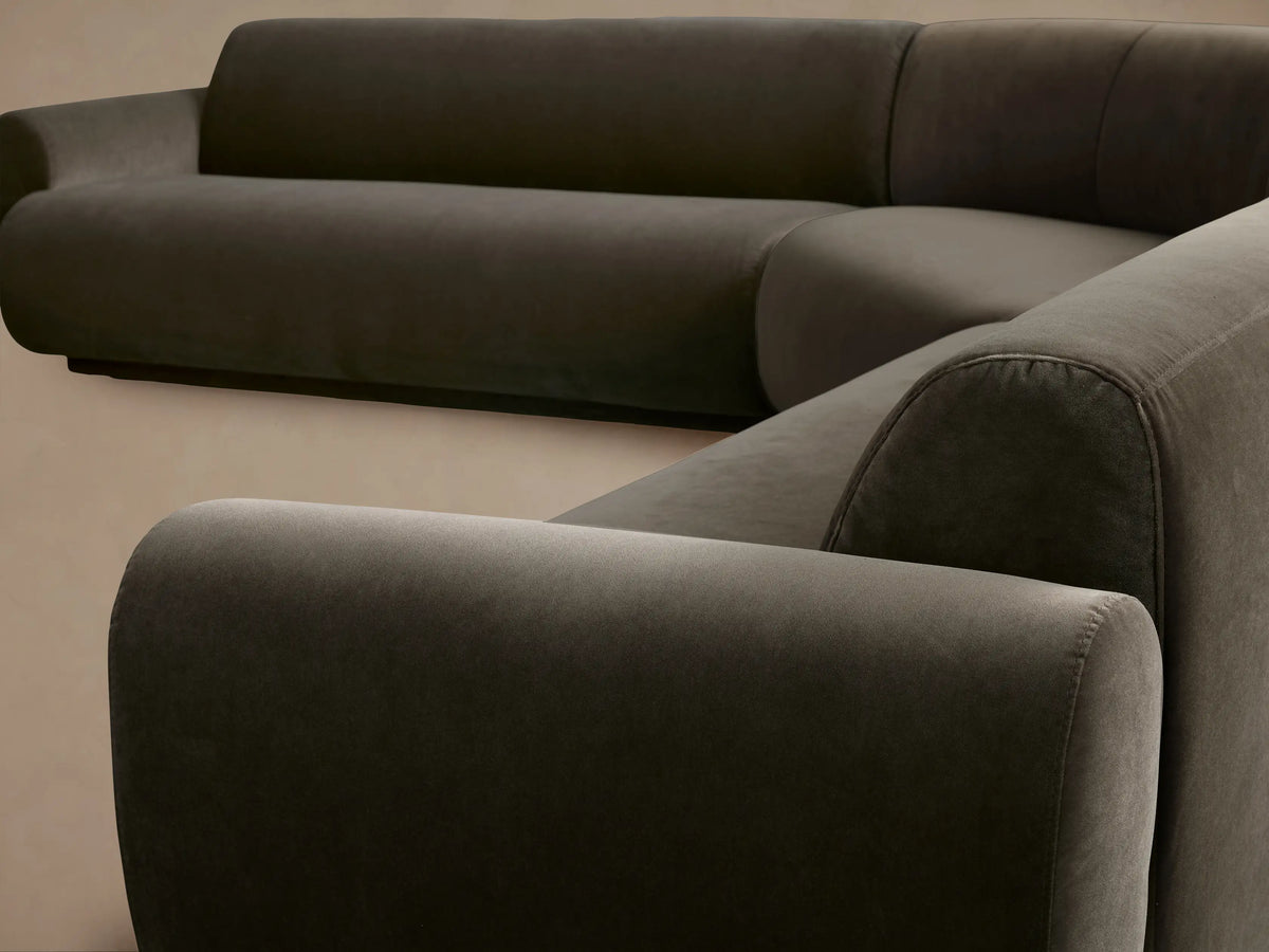 Gianni Three-Piece Corner Sectional in dark grey velvet, L-shaped with rounded armrests, viewed straight on against a tan wall.