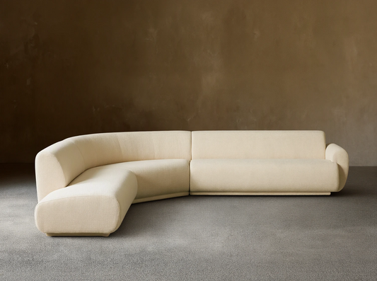 Gianni Three-Piece Bumper Sectional in cream, L-shaped with a curved left end, on a wood floor against a beige wall.