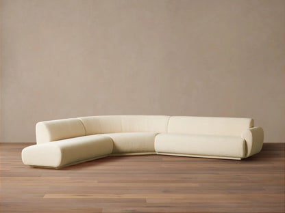 Gianni Three-Piece Bumper Sectional in cream, L-shaped with a curved left end, on a wood floor against a beige wall.