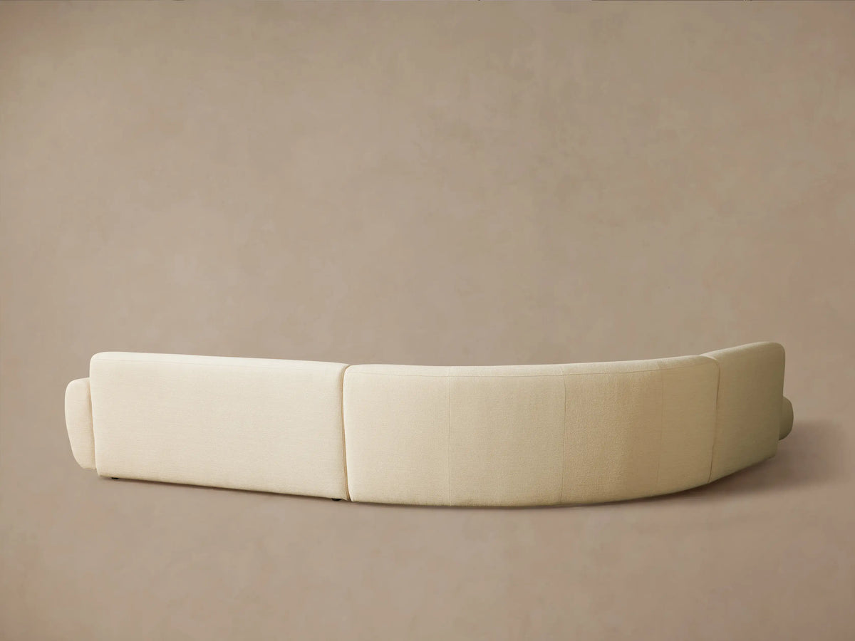 Gianni Three-Piece Bumper Sectional with a curved design, upholstered in cream-colored, textured fabric, from an aerial view.