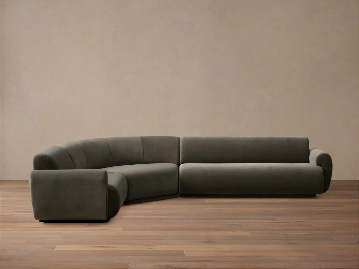 L-shaped Gianni Three-Piece Sectional, dark grey velvet, featuring a curved corner and a straight section with a rolled arm.