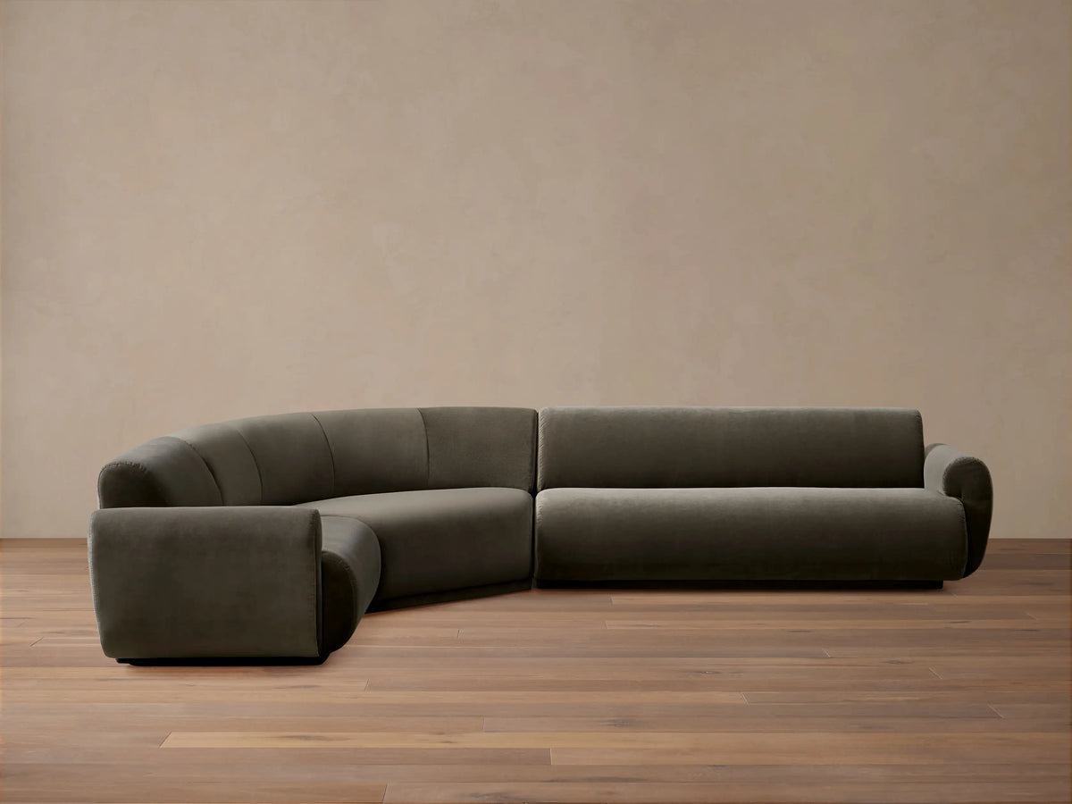 Close-up of a curved Gianni Three-Piece Sectional sofa in dark grey velvet, showing the channel-tufted back.