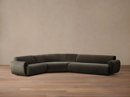 Curved Gianni Three-Piece Sectional in dark olive-gray, viewed from the back against a minimalist beige wall.