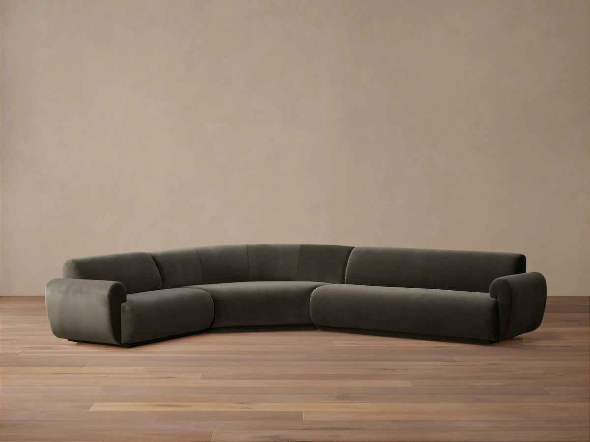 Deep taupe Gianni Three-Piece Sectional with a distinctive curved design, featuring multiple throw pillows, arranged in a spacious room.