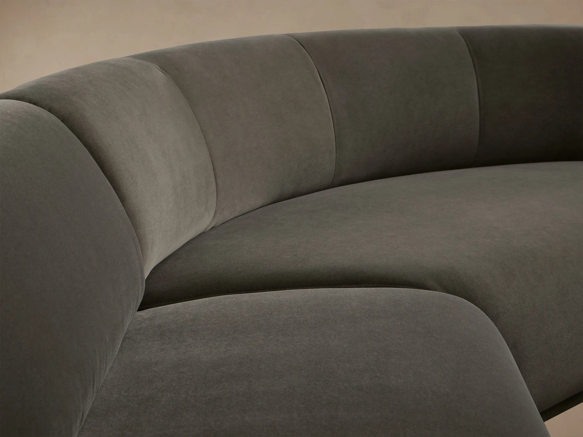 Gianni Three-Piece Sectional, dark charcoal velvet, curved L-shaped sofa on a wooden floor against a beige wall.