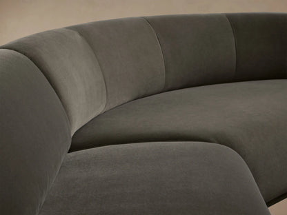 Gianni Three-Piece Sectional, dark charcoal velvet, curved L-shaped sofa on a wooden floor against a beige wall.
