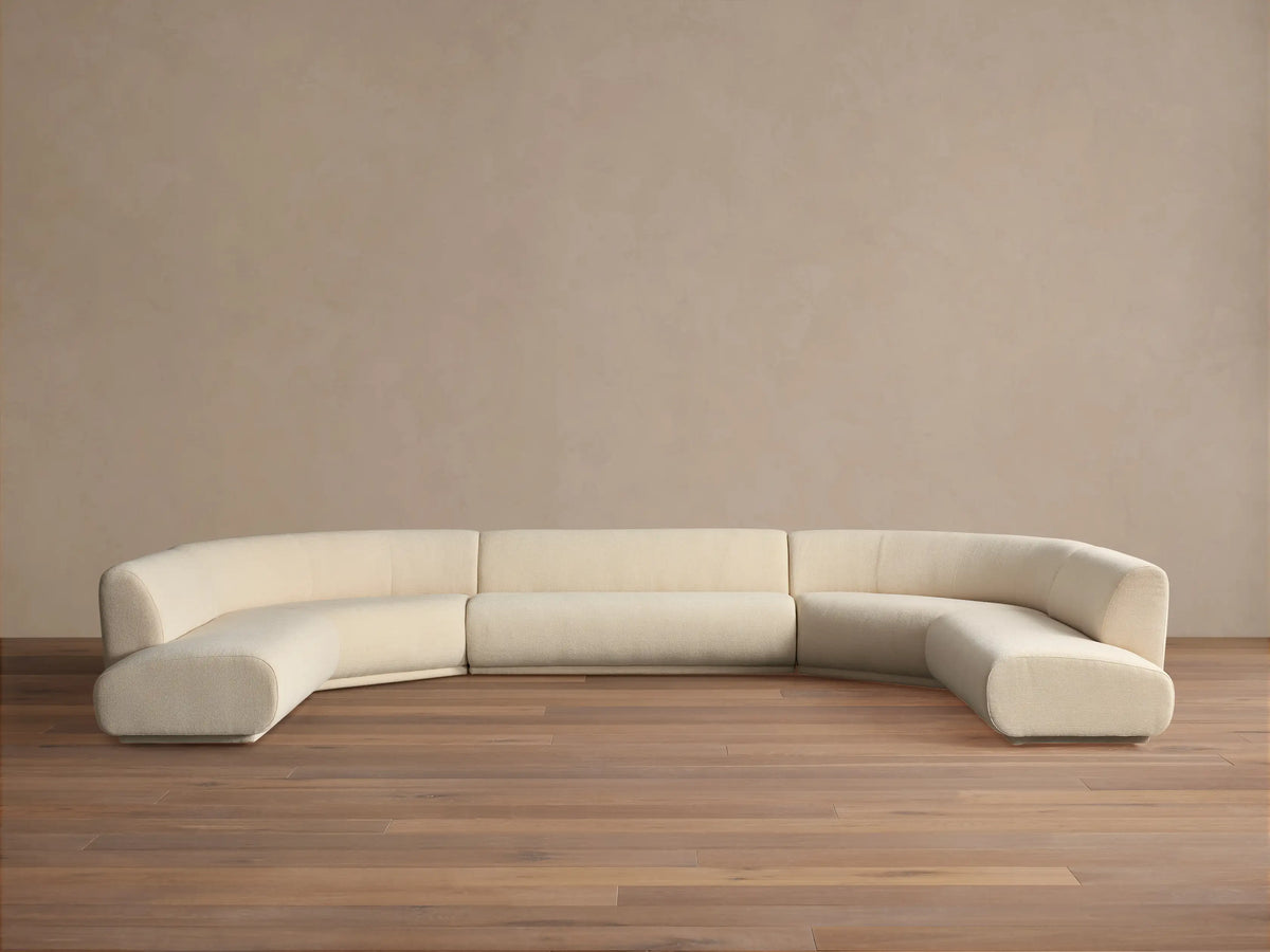 Cream Gianni Five-Piece Curved Bumper Sectional, low-profile and modular, on wood floor against a plain wall.