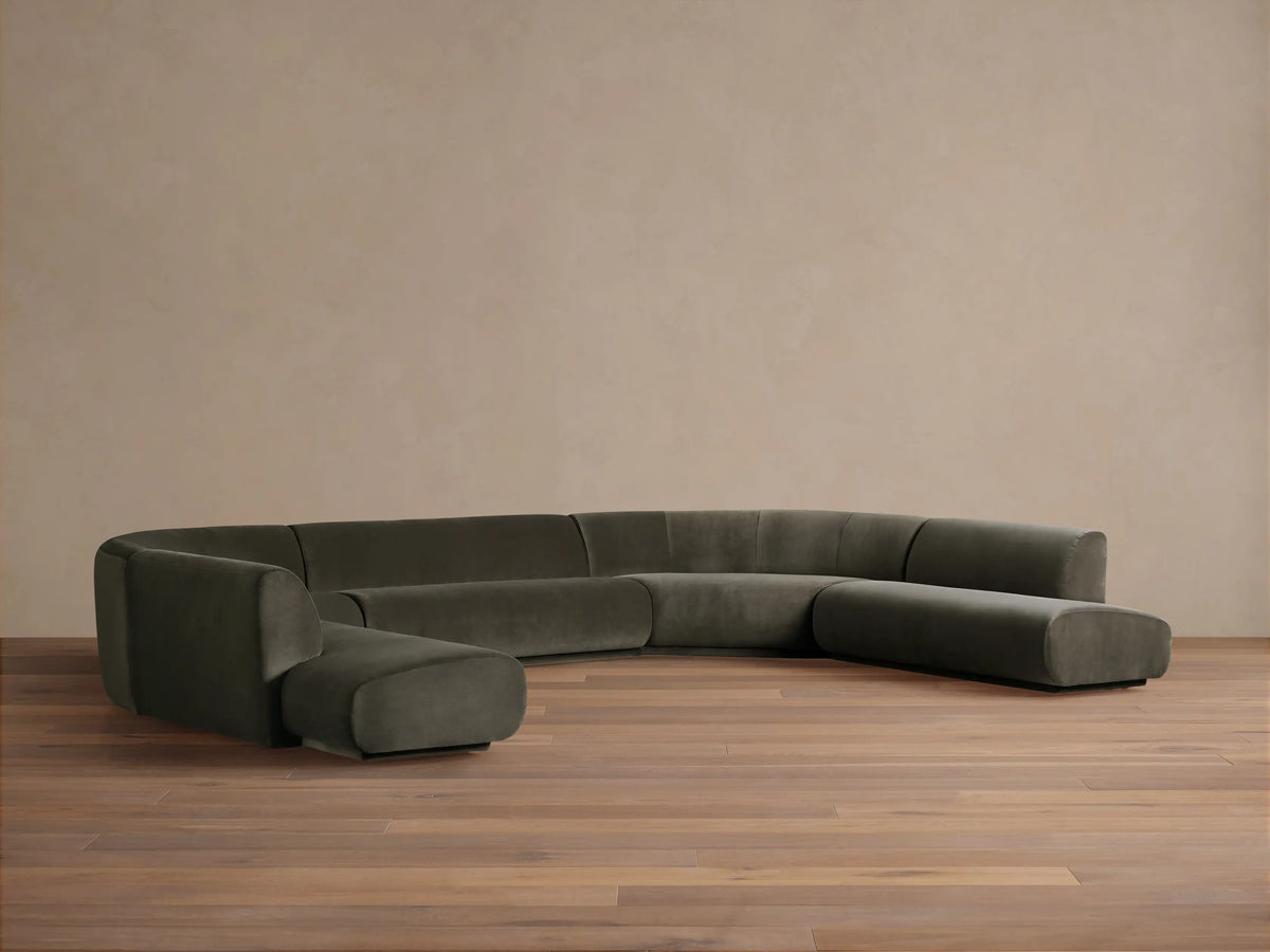 Gianni Five-Piece Curved Bumper Sectional upholstered in deep olive velvet, curving widely on a light wood floor.