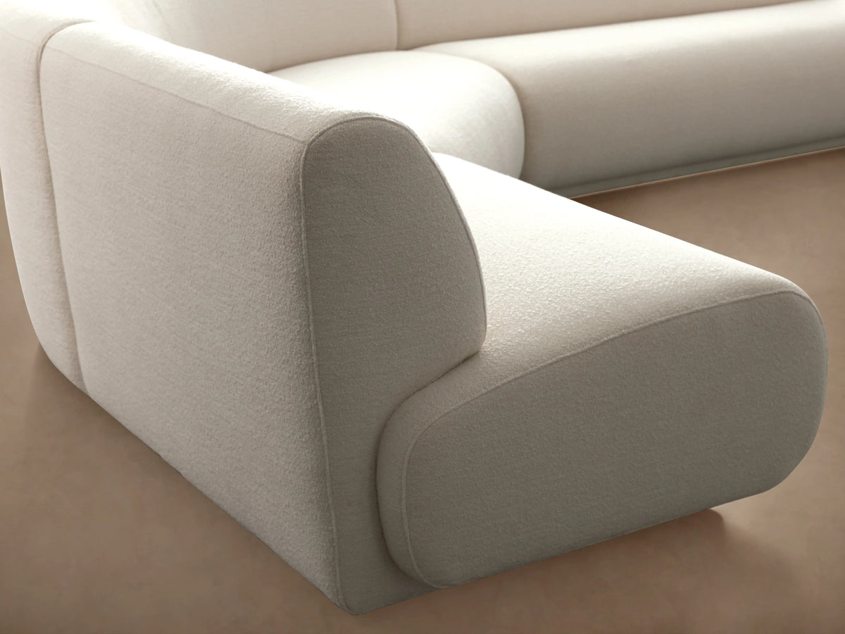 Gianni Three-Piece Sectional in ivory fabric on wooden floor, curved design with plush cushions, against beige wall.