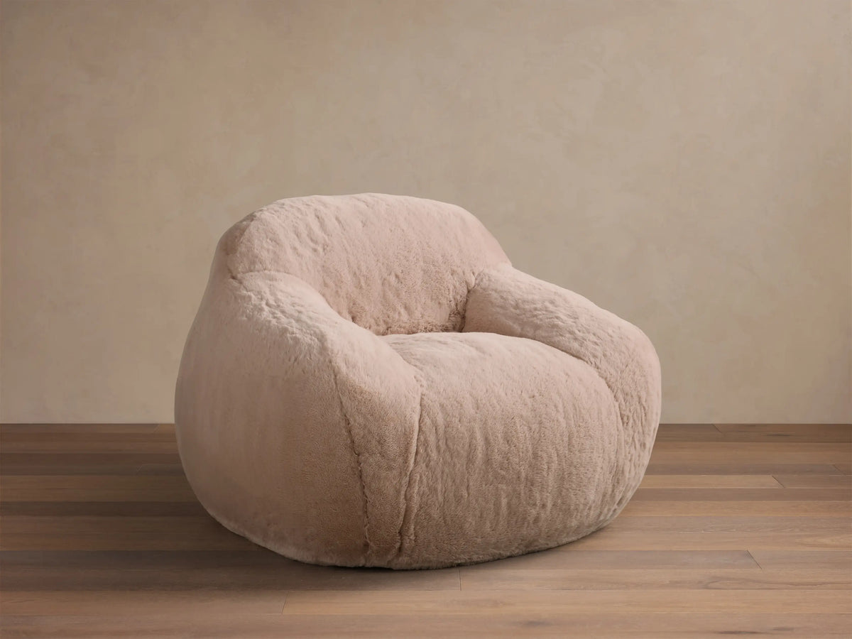Front view of the light pink Snugg Faux Fur Kids Chair, a cozy, generously padded chair on a wooden floor.