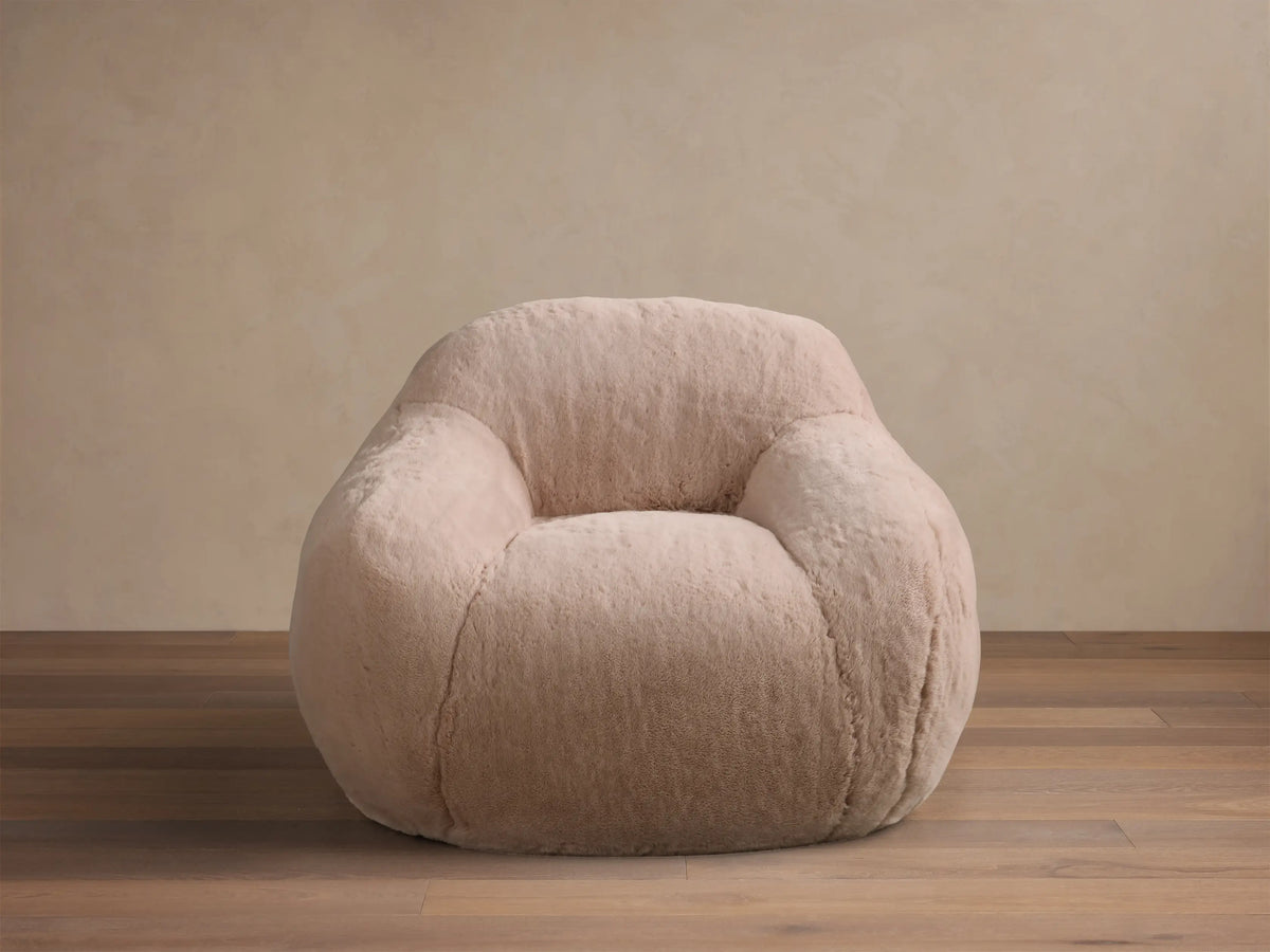 Front view of the light pink Snugg Faux Fur Kids Chair, a cozy, generously padded chair on a wooden floor.