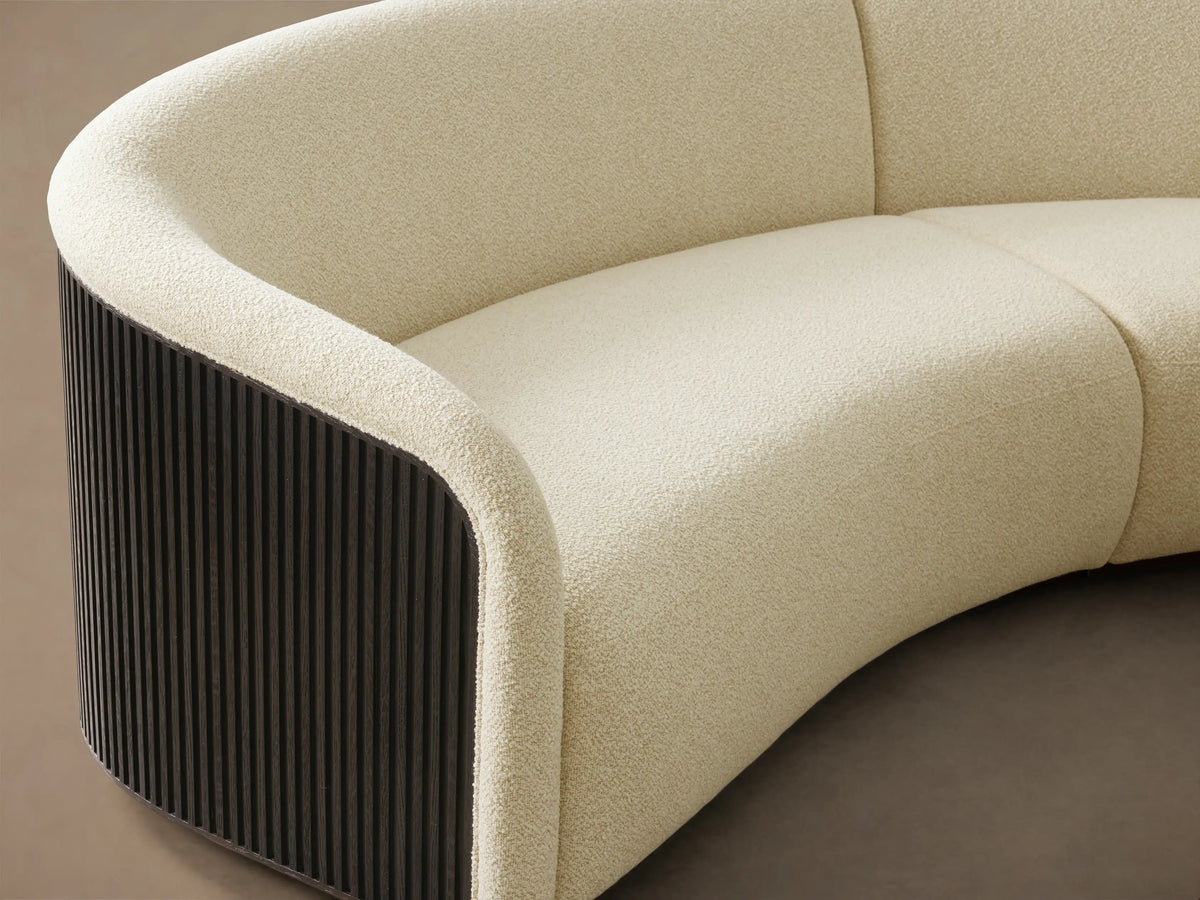 Close-up of the curved Finnley Two-Piece Curved Sectional, upholstered in cream textured fabric with a dark slatted wood panel.