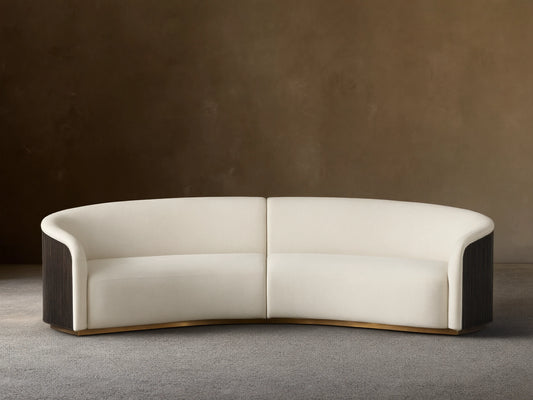 Finnley Two-Piece Curved Sectional in cream fabric, with dark fluted arm ends, and a golden base, on a wood floor.