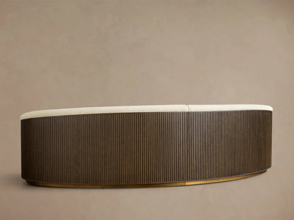 Rear view of the Finnley Two-Piece Curved Sectional, showing a cream upholstered backrest, a curved dark wood slatted base, and a gold trim.
