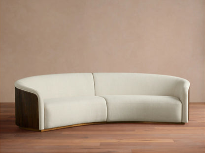 Finnley Two-Piece Curved Sectional sofa in off-white fabric, with dark wood slatted arms, on a wood floor against a warm beige wall.