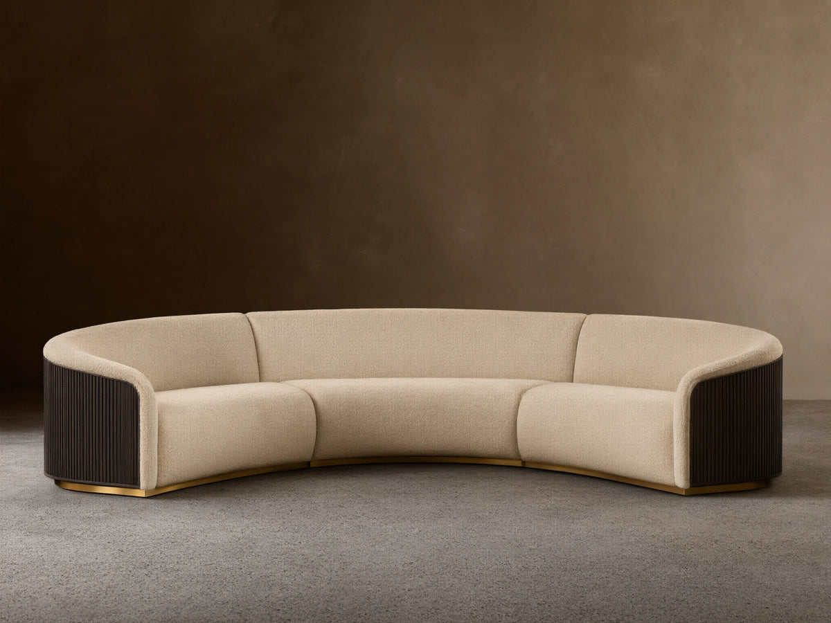 Front view of an Ecru Finnley Three-Piece Curved Sectional with black slatted armrests and a golden base.