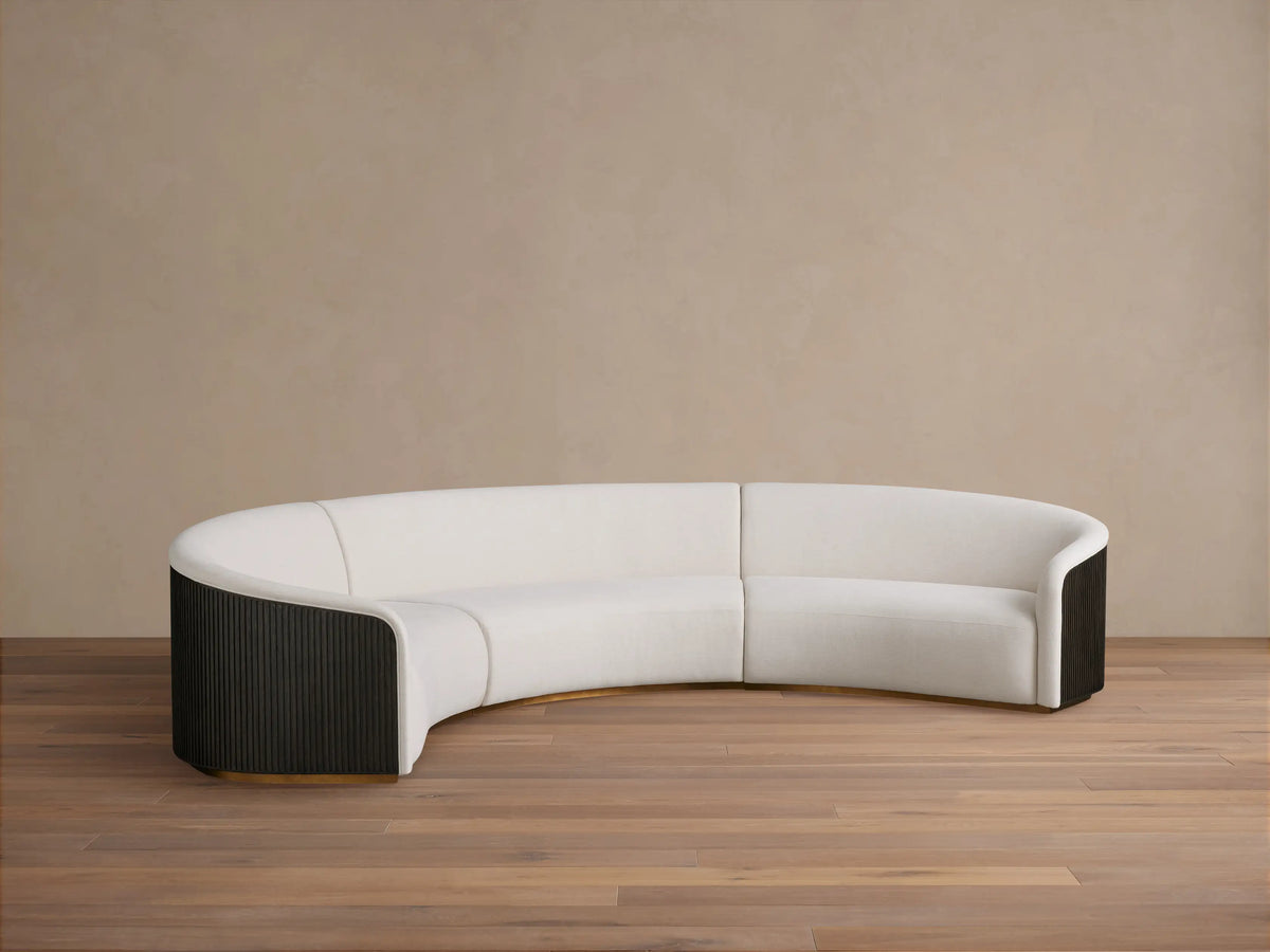 Finnley Three-Piece Curved Sectional in white fabric with dark wood ends and curved design on wooden floor, against beige wall.