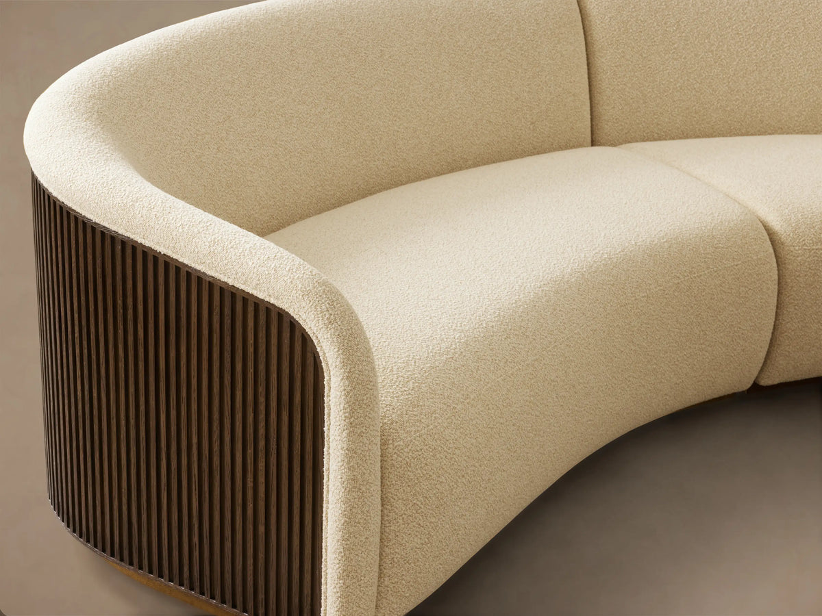 Front view of the cream Finnley Three-Piece Curved Sectional with dark fluted wood side panels and a brass base.