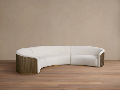Curved three-piece sectional sofa, upholstered in soft white fabric, featuring wooden side panels and positioned on a wooden floor.