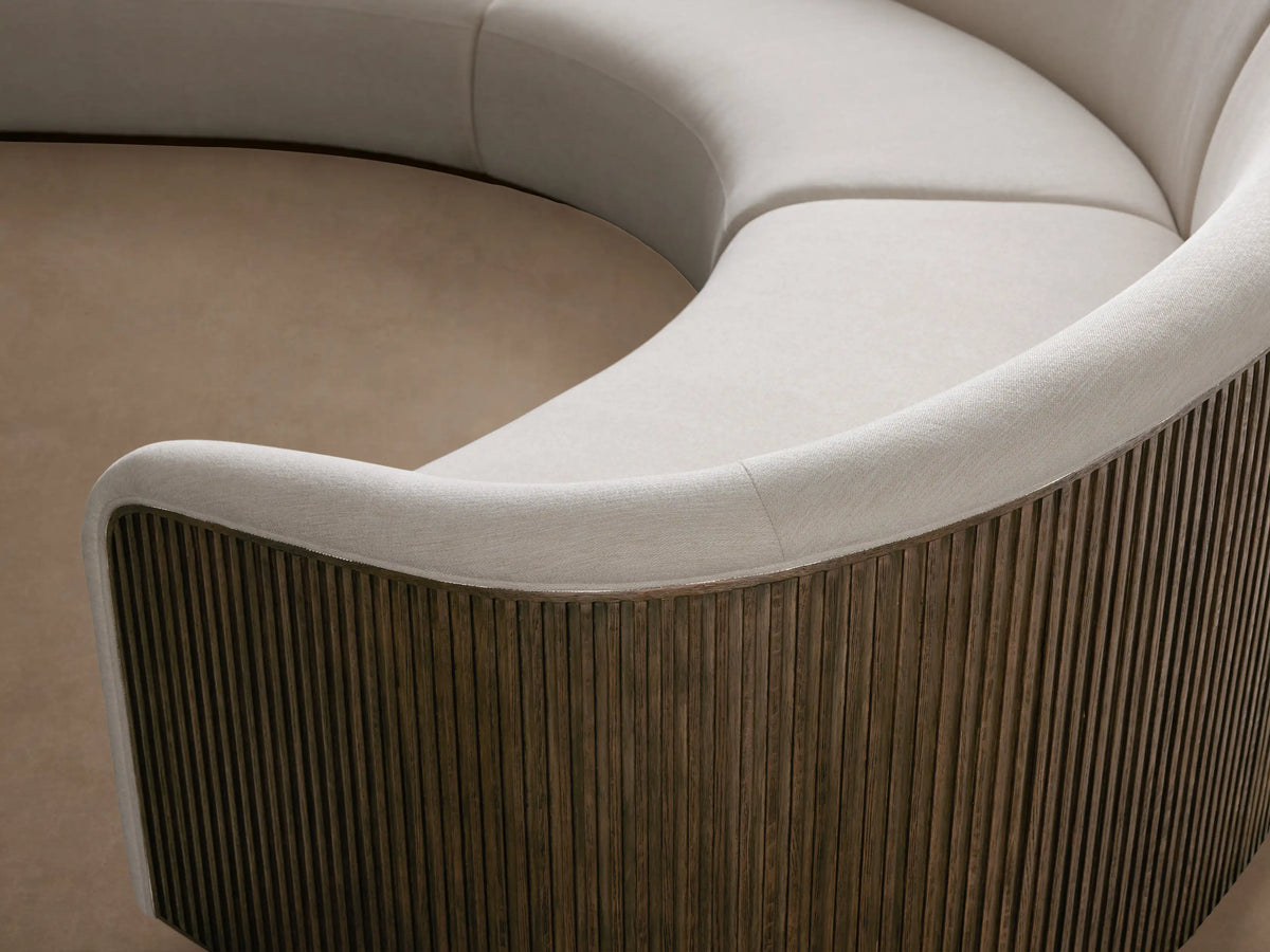 Curved three-piece sectional with white upholstery and wooden veneer sides on both ends. Placed on a wooden floor against a neutral wall.
