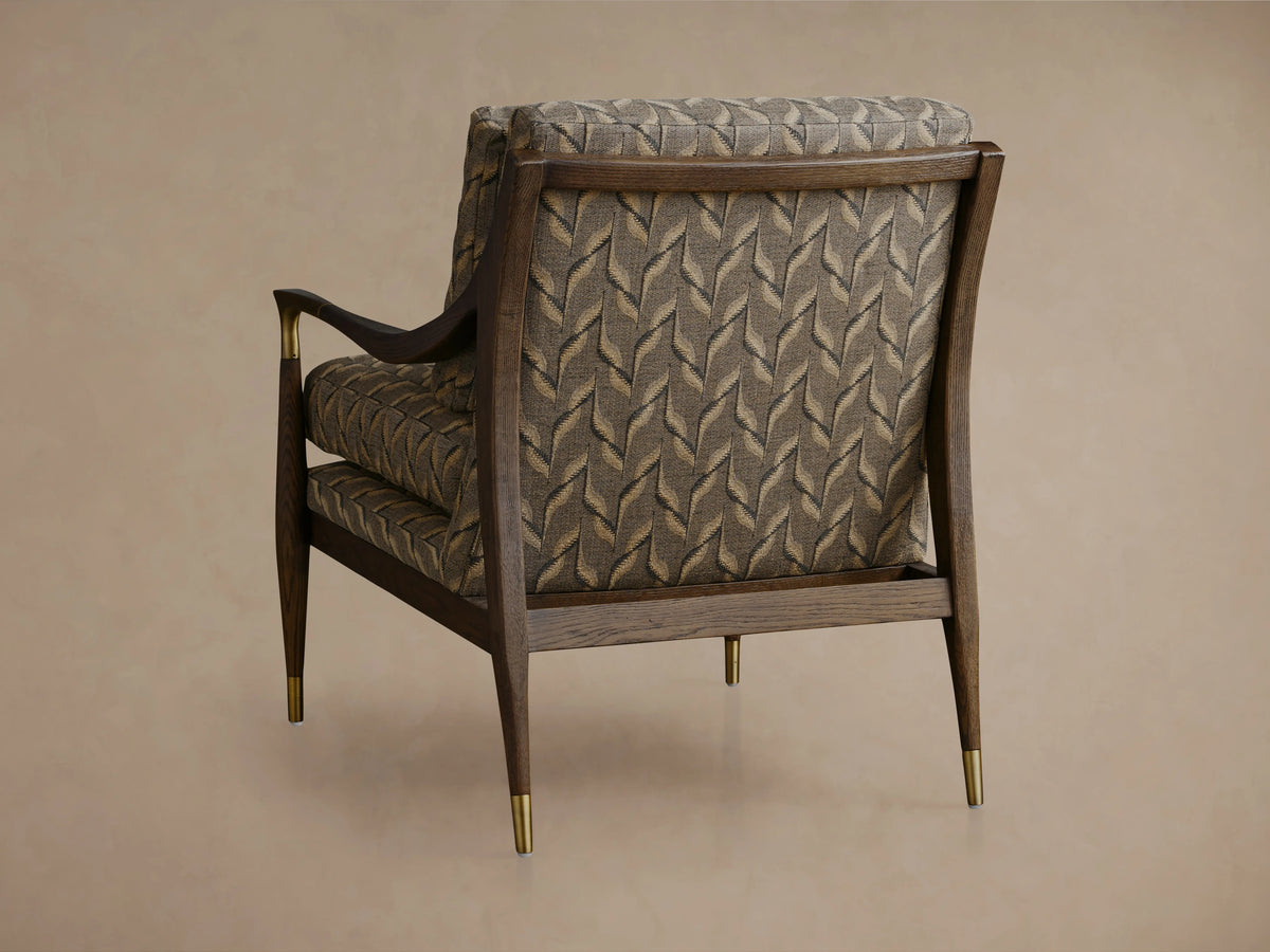 Fisher Chair close-up. Dark mocha wood & brass armrest with intricate grey & beige leaf-patterned fabric upholstery.