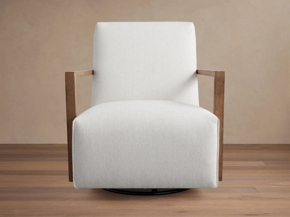 Walsh Glider with a white cushioned seat and back, featuring wooden armrests. Set on a circular swivel base, positioned on a wooden floor.