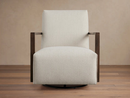 Walsh Glider in light beige fabric with square wooden arms on a round black swivel base, set against a wooden floor.