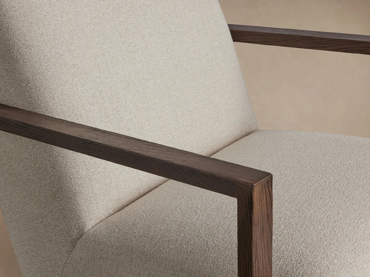 Walsh Glider chair with beige fabric upholstery, wooden armrests, and a round base for swiveling, on a wooden floor.