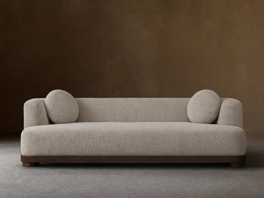 Marcela Sofa in beige upholstery against a neutral wall, featuring rounded armrests and two circular cushions, on a wooden floor.