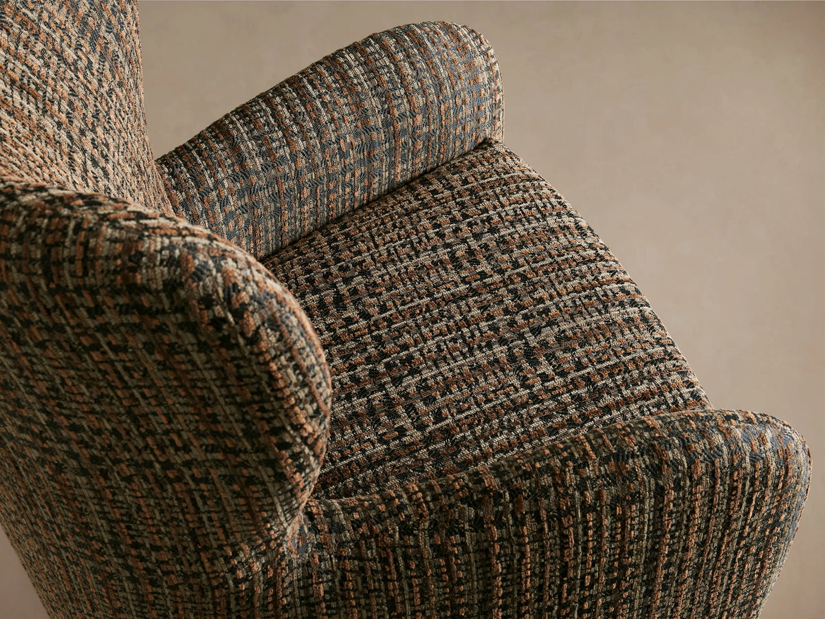 Gemma Swivel Chair with a high backrest and wide armrests upholstered in a textured, multicolored fabric, on a wooden floor.