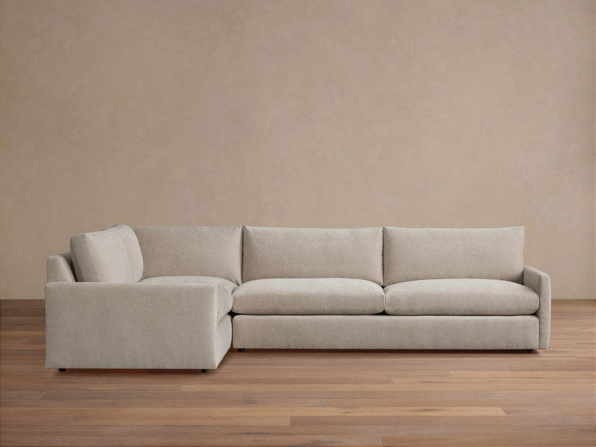 Kipton Two-Piece Sectional in beige fabric, featuring a left-arm chaise and right-arm sofa. Set on a wooden floor, against a plain beige wall.