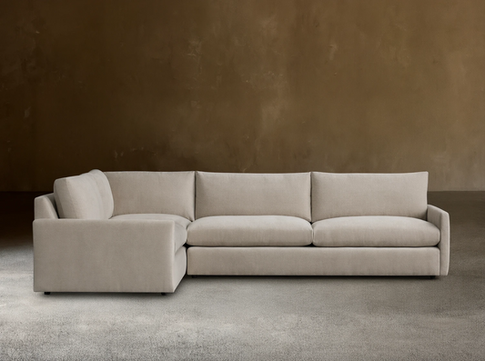 Kipton Two-Piece Sectional in beige fabric, featuring a left-arm chaise and right-arm sofa. Set on a wooden floor, against a plain beige wall.