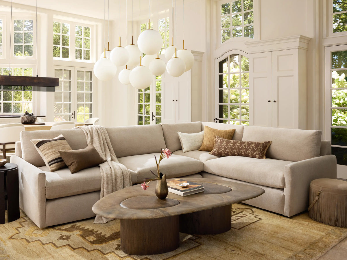 Front view of the Kipton Slim Arm Two-Piece Sectional in a light beige fabric, with throw pillows and a blanket, in a bright living room.