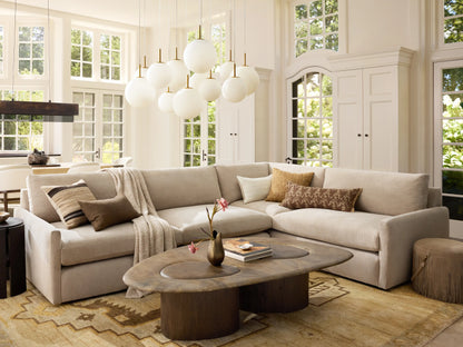 Front view of the Kipton Slim Arm Two-Piece Sectional in a light beige fabric, with throw pillows and a blanket, in a bright living room.