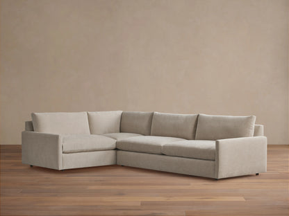 Kipton Two-Piece Sectional in beige fabric, featuring a left-arm chaise and right-arm sofa. Set on a wooden floor, against a plain beige wall.