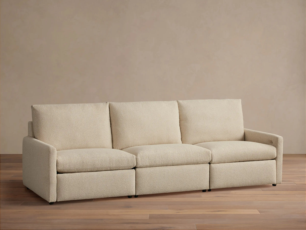 Kipton Three-Piece Motion Modular Sofa in beige fabric, shown in a simple, modern room. Three cushioned seats and slim arms.