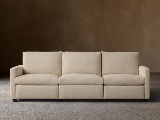 Kipton Three-Piece Motion Modular Sofa in beige fabric, shown in a simple, modern room. Three cushioned seats and slim arms.