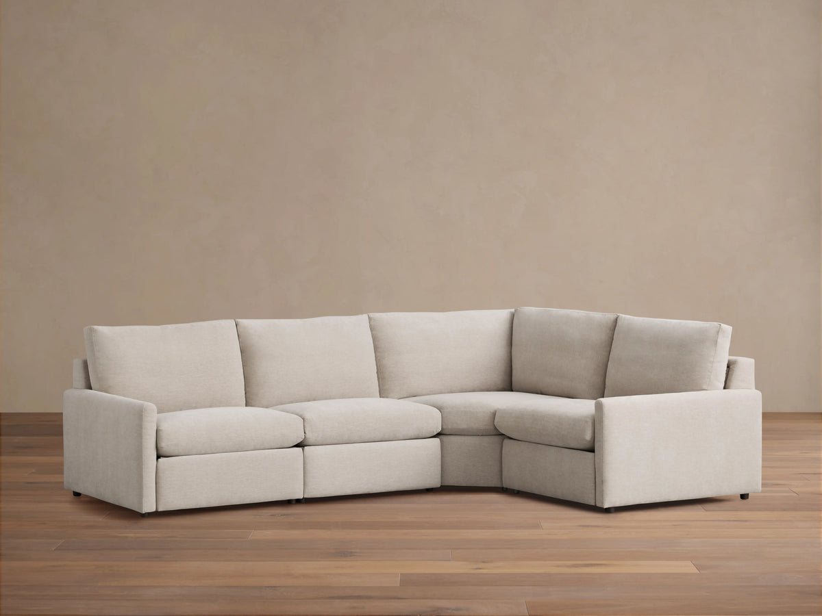 Kipton Four-Piece Motion Sectional in beige fabric, shown in a right-angle configuration on a wooden floor, with slim arms and cushioned seats.