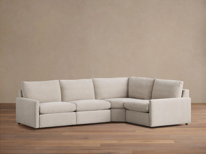 Kipton Four-Piece Motion Sectional in beige fabric, shown in a right-angle configuration on a wooden floor, with slim arms and cushioned seats.