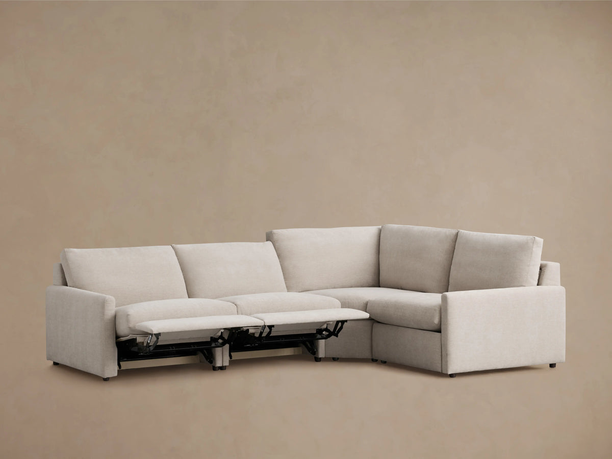 The Kipton Four-Piece Motion Sectional in a soft beige fabric features straight, slim arms and cushioned backrests against a beige wall.