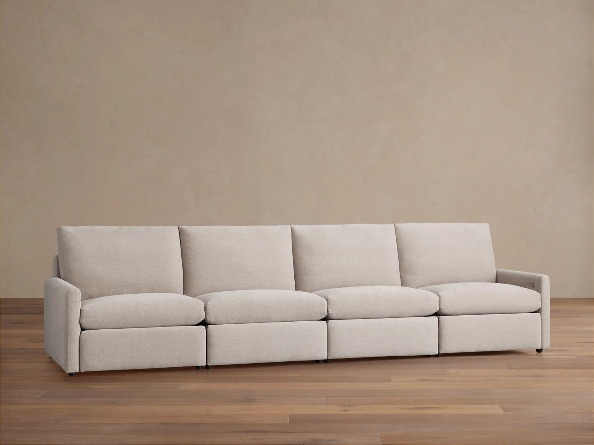 Kipton Four-Piece Motion Modular Sofa, light beige fabric, slim arms, four seats, and high backrests on wooden floor against a beige wall.