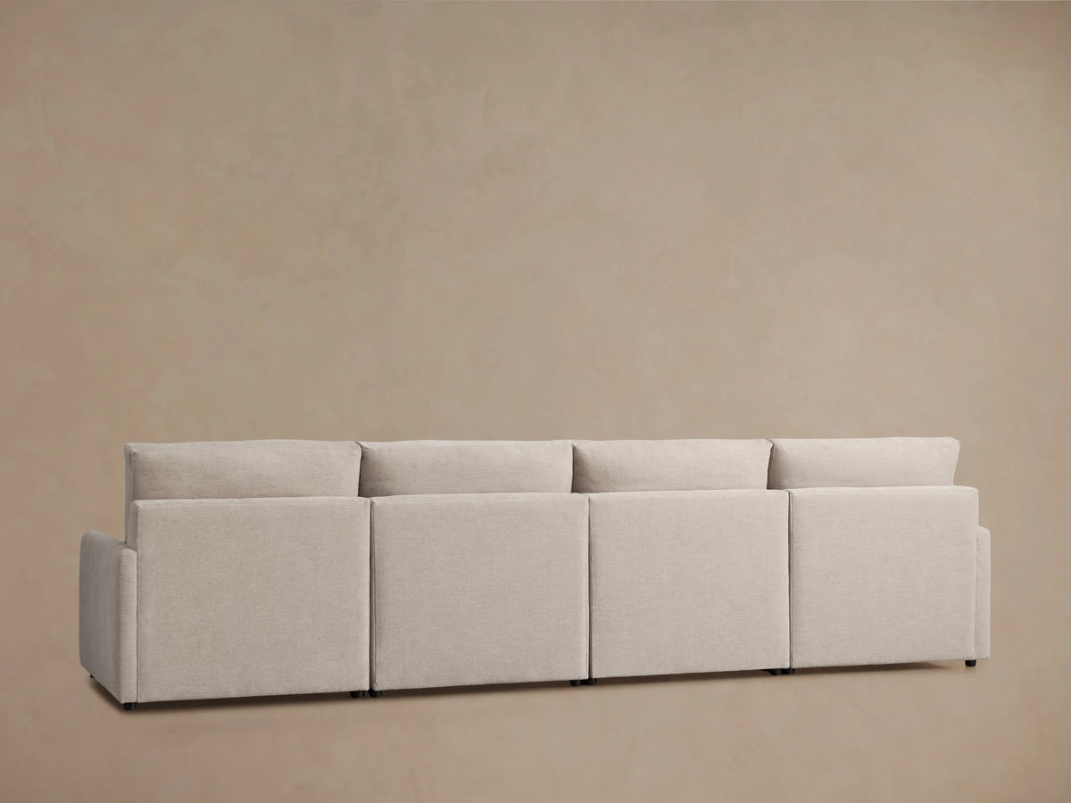 Light beige Kipton Four-Piece Motion Modular Sofa close-up showing the right armrest with a reclining button and footrest extended on a tan floor.