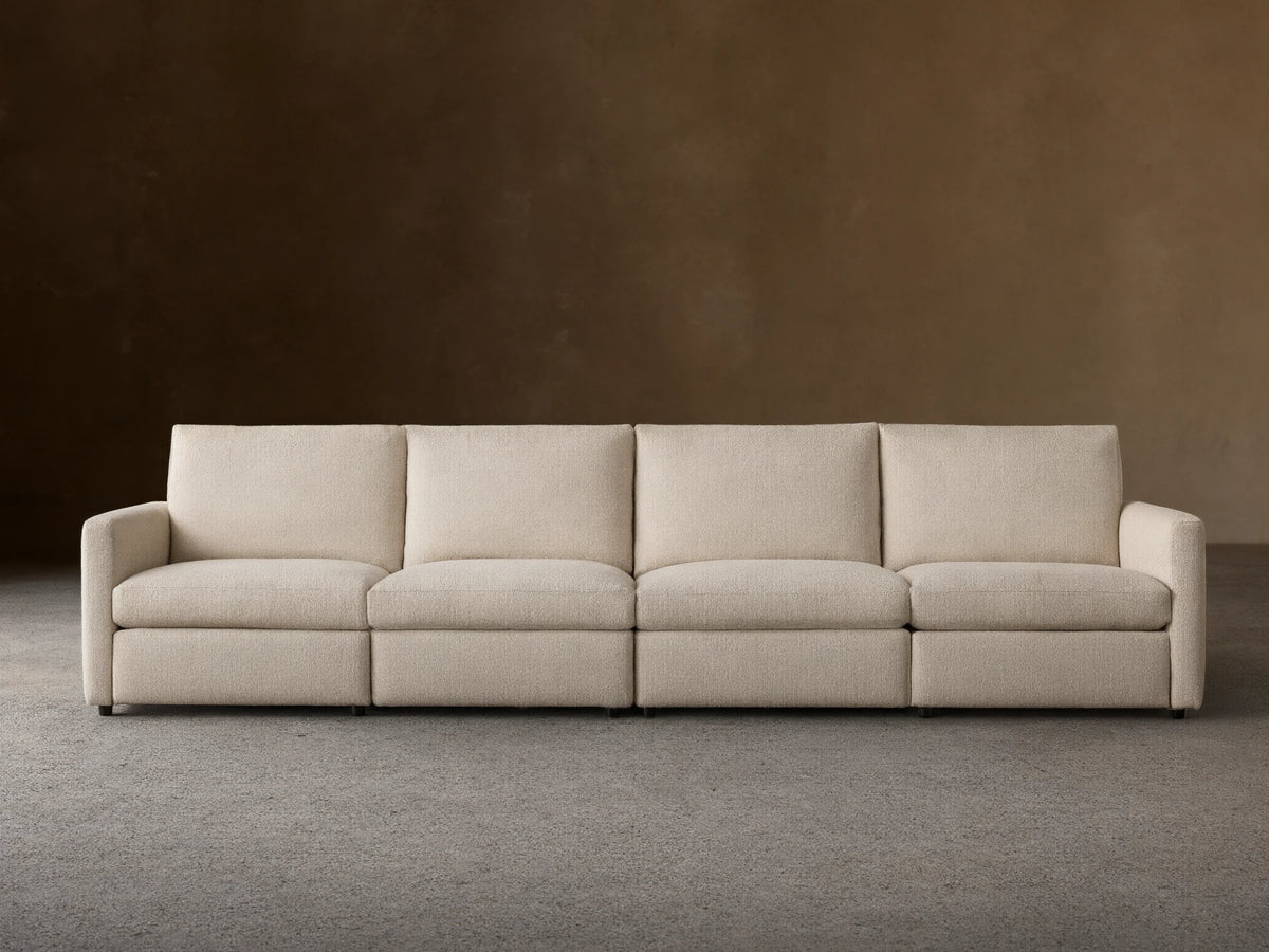 Kipton Four-Piece Motion Modular Sofa in beige fabric, viewed from the front. Features slim arms, four cushioned seats, and backrests, on a wooden floor.