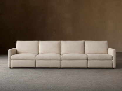 Kipton Four-Piece Motion Modular Sofa in beige fabric, viewed from the front. Features slim arms, four cushioned seats, and backrests, on a wooden floor.