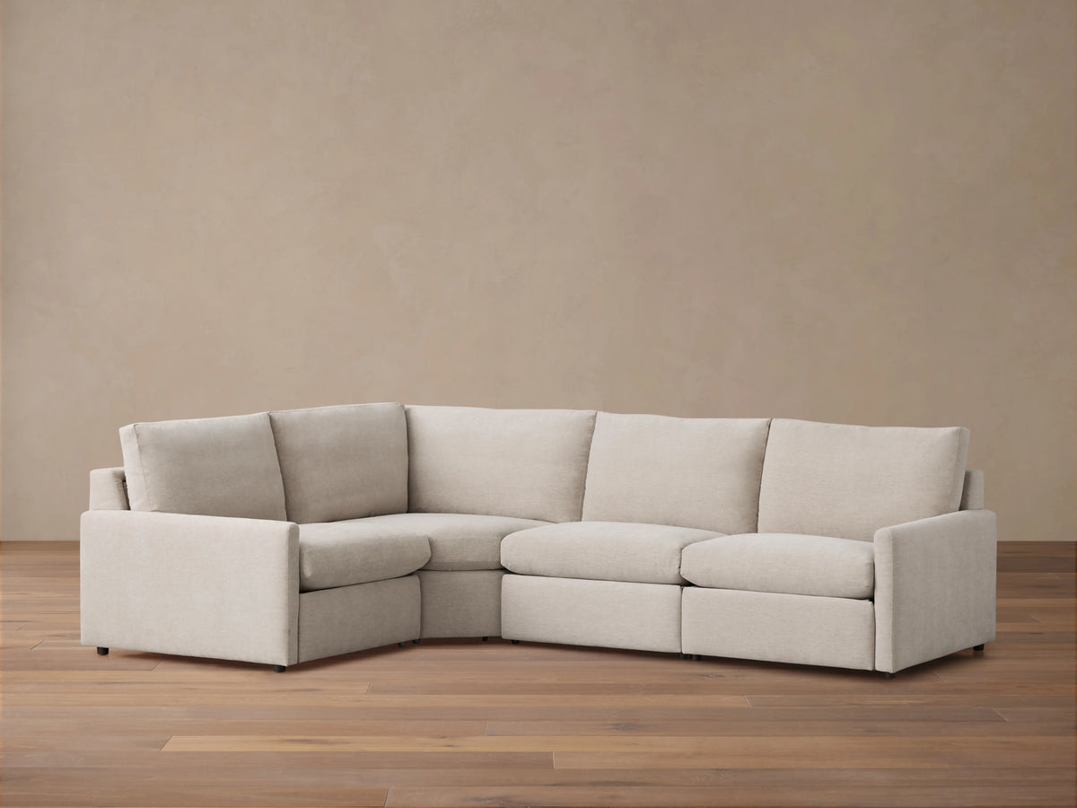 Kipton Four-Piece Motion Sectional in light beige fabric, arranged in an L-shape on a wooden floor, featuring slim arms and cushioned backs.