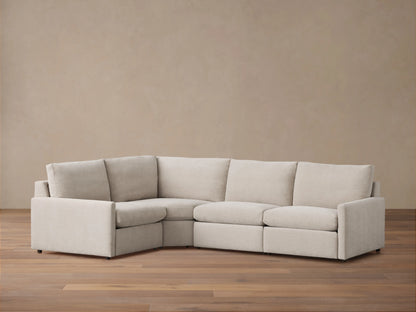 Kipton Four-Piece Motion Sectional in light beige fabric, arranged in an L-shape on a wooden floor, featuring slim arms and cushioned backs.
